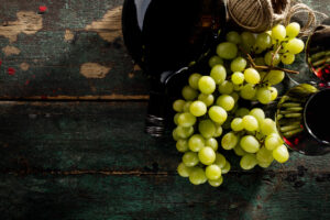 garrafa de vinho tinto e uvas verdes em cima de uma mesa rústica de madeira 