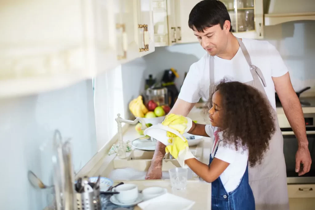 Pai e filha lavando a louça durante a limpeza da casa 