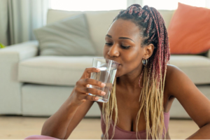 Mulher na sala de casa tomando um copo d'água