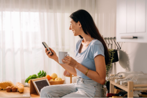 Mulher sorridente enquanto toma uma xícara de café e mexe em seu celular