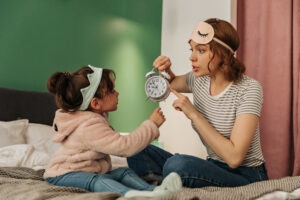 Mãe e filha sentadas na cama olhando pra despertador 