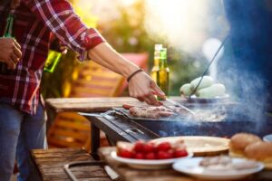 Um momento especial de Dia dos Pais, com um pai preparando um churrasco ao ar livre, cercado por amigos e familiares, enquanto saboreiam bebidas e delícias na grelha.
