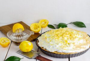 Uma deliciosa torta de limão, decorada com fatias de limão e acompanhada por limões frescos, ideal para um almoço de Dia dos Pais.