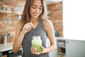 Mulher tomando um suco verde feito com suplementos para veganos