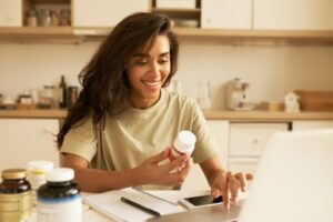 Mulher sorridente analisando um frasco de vitaminas enquanto escolhe suplementos e vitaminas em sua mesa.