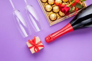 Champanhe com algumas taças e caixa de chocolates, exemplo de presentes de fim de ano.