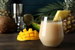 Copo servido com drink tropical em meio a frutas tropicais.