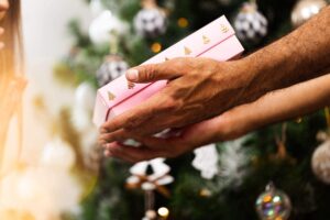 Mão entregando um presente de natal, representando um gesto solidário.