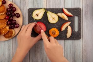 Imagem de cima de uma pessoa cortando frutas frescas.