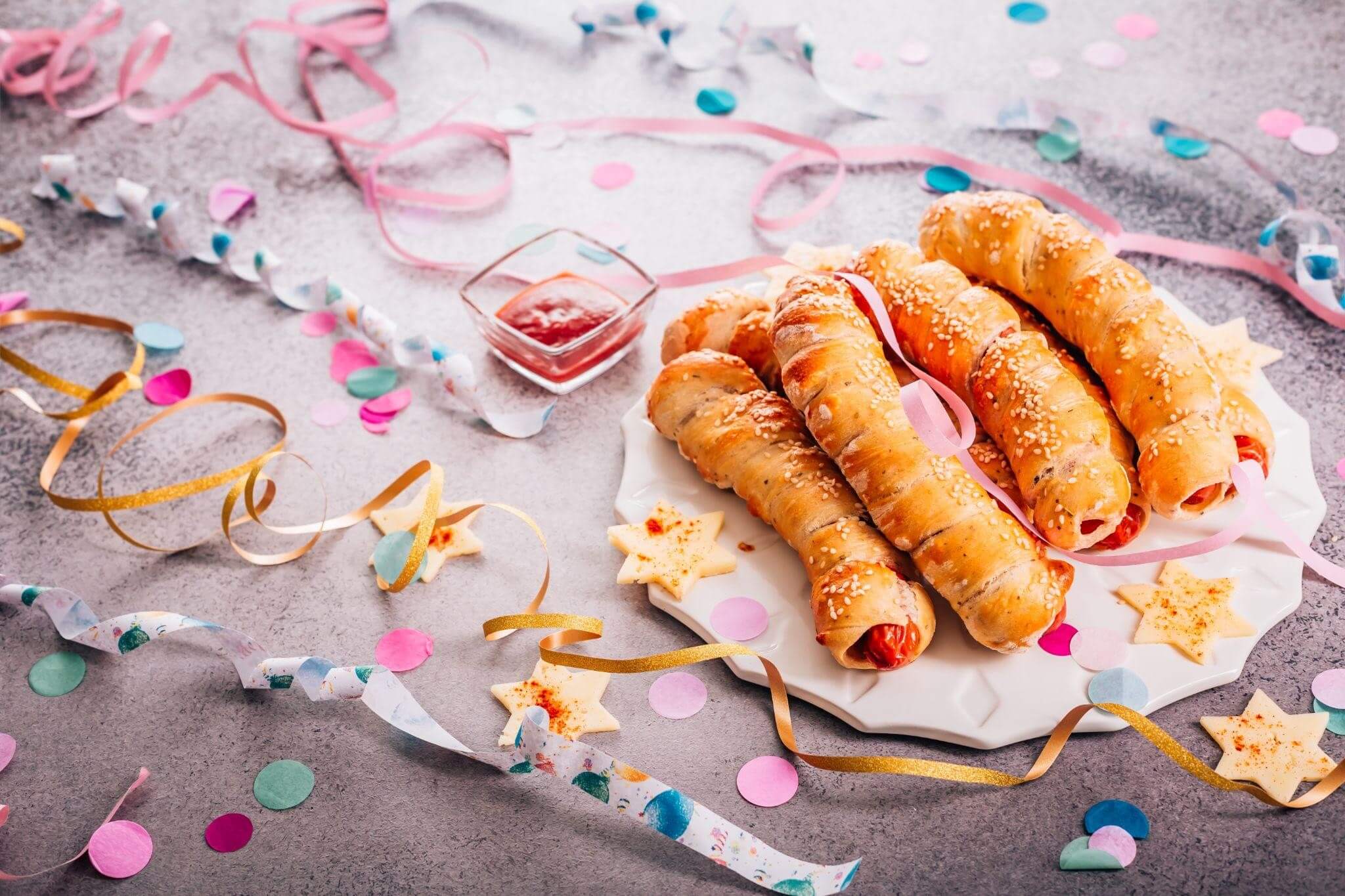 Lanches folhados recheados em um prato com decorações e confetes em sua volta.