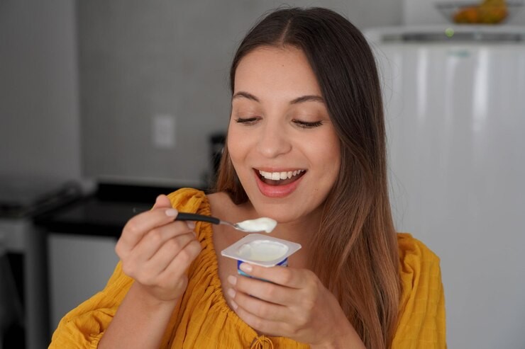 Uma mulher sorridente aproveitando os benefícios do iogurte ao consumi-lo no café da manhã.