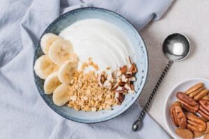 Uma tigela com iogurte, granola, castanhas e bananas. 