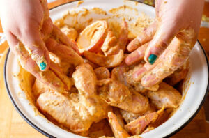 Mãos femininas marinando frango, jeito certo de como temperar carne branca para churrasco. 