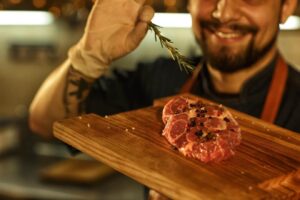 Homem segurando tábua com carne vermelha temperada para churrasco. 