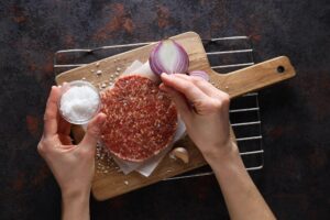 Mulher temperando hamburguer gourmet em casa. 