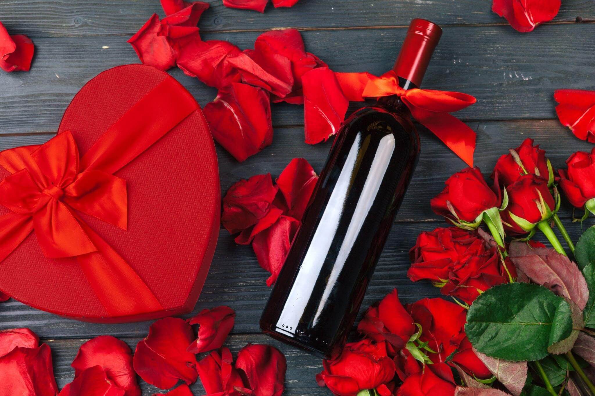 Garrafa de vinho tinto ao lado de uma caixa de bombom e rosas vermelhas para o Dia dos Namorados.