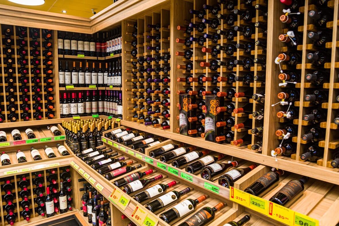 Exposição de uma grande variedade de vinhos armazenados em prateleiras de madeira na Feira Itinerante de Vinhos Covabra 2025, com destaque para a diversidade de garrafas disponível para amantes de vinhos e colecionadores durante o evento.