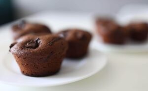 Muffins de chocolate fofos e brilhantes em um prato branco, uma das muitas receitas com creme de avelã que podem ser feitas para o lanche.